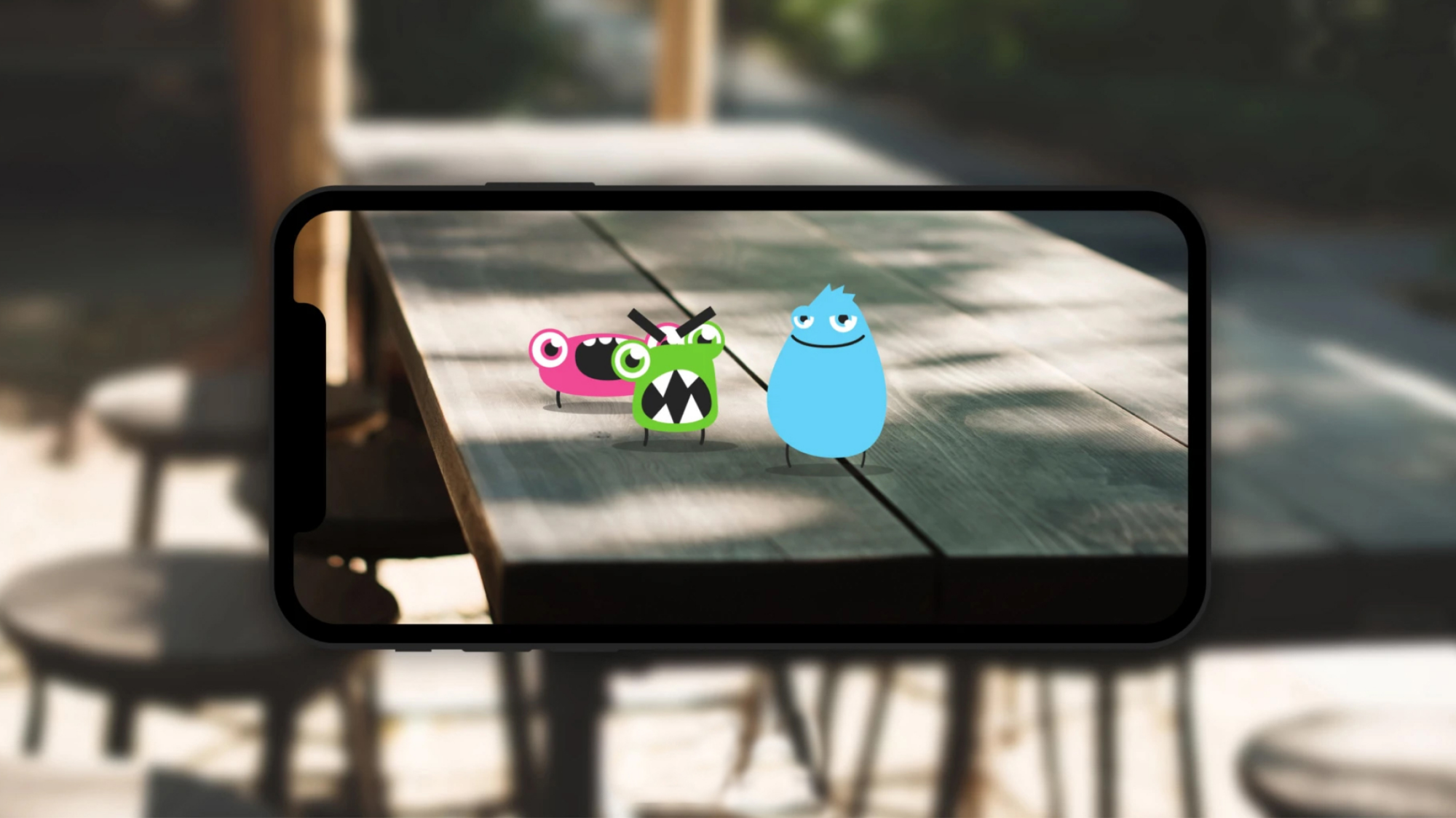 Three cartoon-like characters—one pink, one green, one blue—stand on a table, bringing life to the new iPlayer Kids brand.