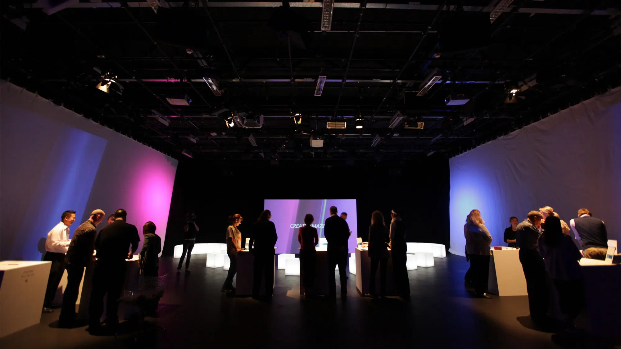 A group of people stand in a room, looking at laptops in front of a screen with the title 