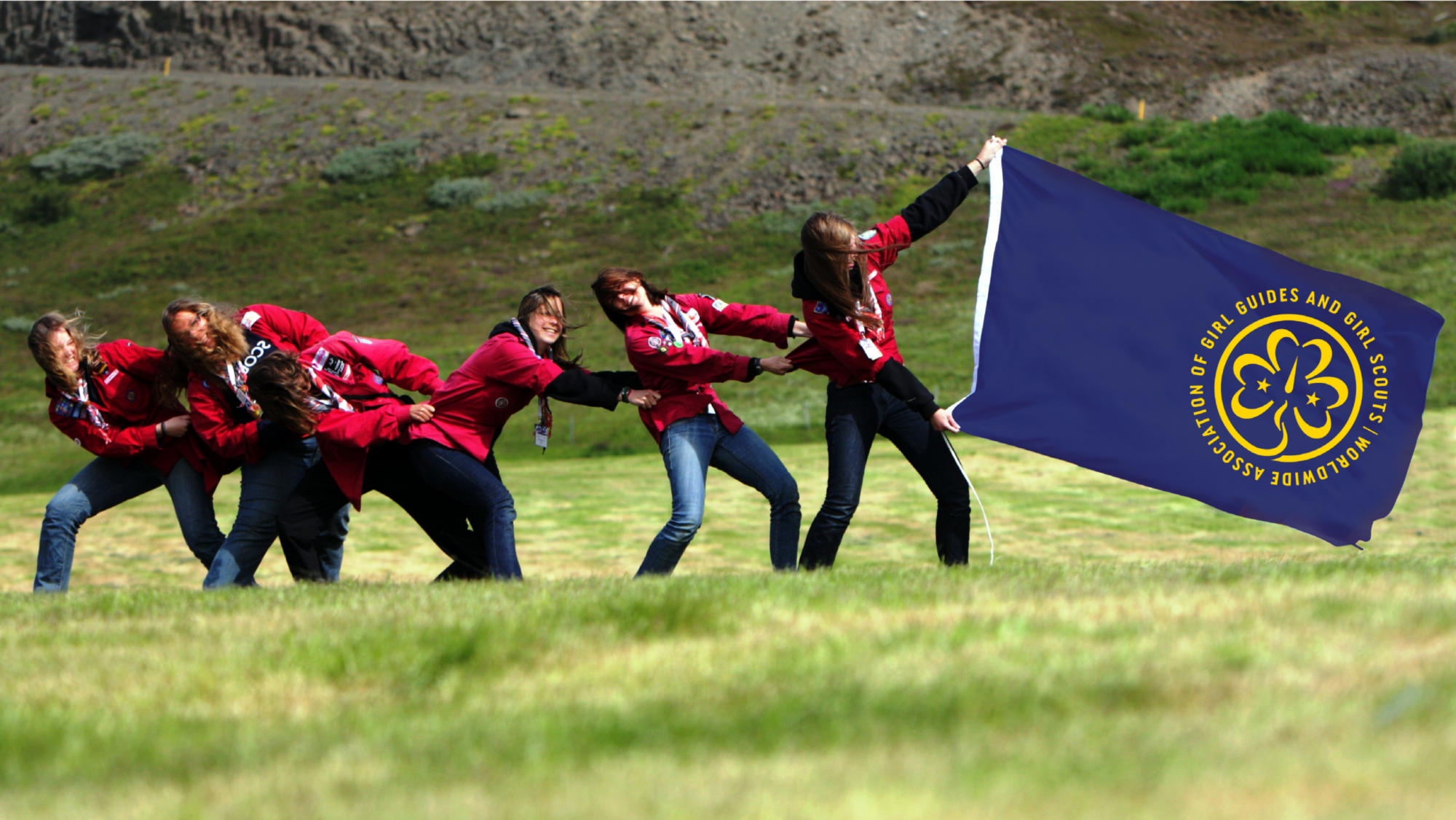 A line of Girl Guides holding the World Association of Girl Guides and Girl Scouts flag.