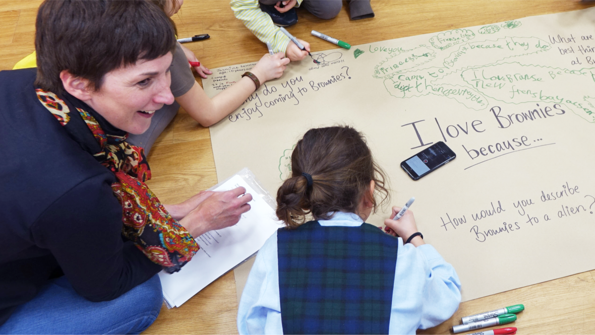 A group of children are writing on a large piece of paper, saying why they love going to Brownies.